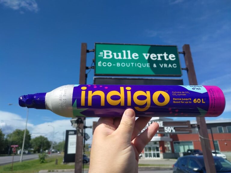 Une main tient une bonbonne de CO2 Indigo devant un magasin La Bulle Verte. La bonbonne indique "Cylindre de CO2" et "Donne jusqu'à 60L".