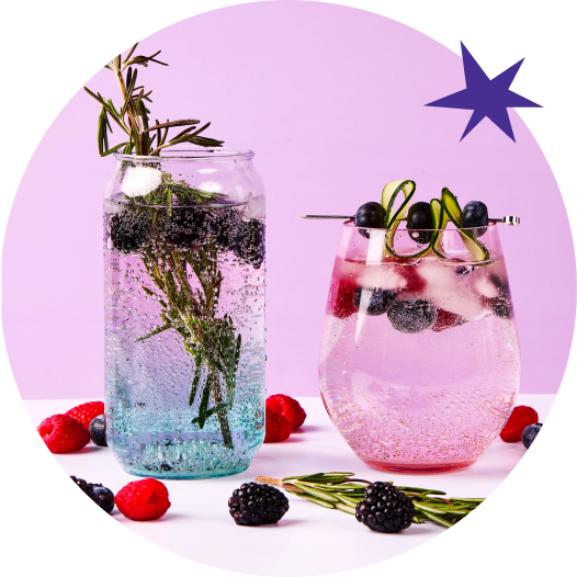 Deux verres remplis d'une boisson pétillante rose clair avec des glaçons, des bleuets, des framboises, des mûres et du romarin. Les verres sont posés sur une table avec des bleuets, des framboises, des mûres et du romarin éparpillés autour. Le fond est mauve avec une étoile bleue dans le coin supérieur droit.